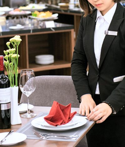 Restaurant staff in formal attire setting a clean, elegant dining table with wine, flowers, and dinnerware.